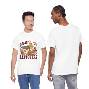 May include: A white short-sleeve t-shirt featuring a graphic of a food container, a slice of pumpkin pie, and autumn leaves with the text "GRATEFUL FOR LEFTOVERS" in dark red lettering. The back of the t-shirt is plain white.