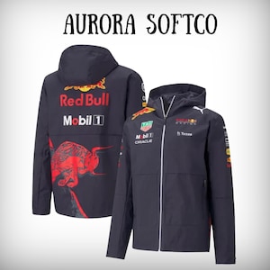 May include: A navy blue hooded jacket with the Red Bull Racing logo and sponsor logos. The back of the jacket features a large red bull graphic and the text "Red Bull Mobil 1". The text "AURORA SOFTCO" is at the top.