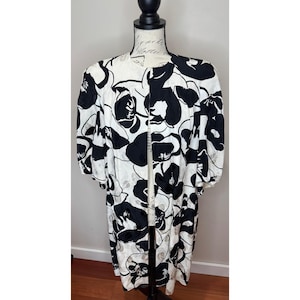 May include: A knee-length open-front duster coat featuring a bold black and white floral pattern. The garment has a round neckline, three-quarter length sleeves with gathered cuffs, and a loose, flowing silhouette made of lightweight fabric.
