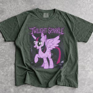 Könnte beinhalten: Dunkelgrünes T-Shirt mit einem Aufdruck von Twilight Sparkle, einem lila Pony mit Horn und Flügeln. Der Text "TWILIGHT SPARKLE" steht in einer stilisierten Schriftart über dem Pony. Das T-Shirt hat einen Vintage-Look.