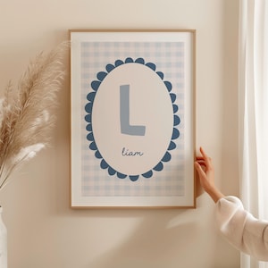 May include: A framed print with a blue and white gingham pattern. A blue circle with a white scalloped border surrounds a large blue letter L and the name "liam" in white text.