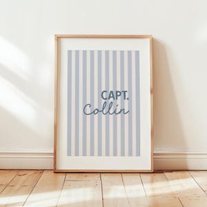 K&ouml;nnte beinhalten: Ein gerahmter Druck mit einem blau-wei&szlig; gestreiften Hintergrund und dem Text "CAPT. Collin" in dunkelblau.