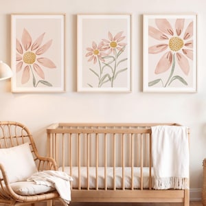May include: Three framed prints featuring watercolour illustrations of pink flowers on a light beige background. The prints are hanging on a white wall above a wooden cot.