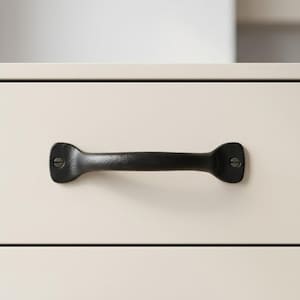 May include: A black, cast iron drawer pull with a textured surface. The handle is a horizontal bar with rounded ends, each secured with a single screw. The pull is mounted on a cream-colored drawer front.