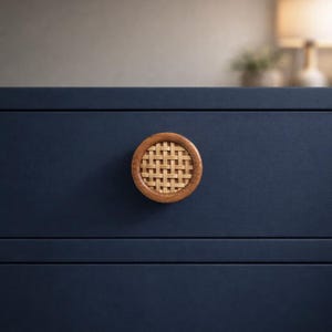 May include: A close-up of a navy blue cabinet drawer with a round wooden knob. The knob features a woven rattan center surrounded by a wooden frame. The cabinet has a clean, modern design.