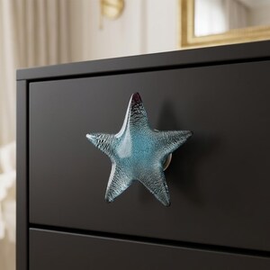 May include: A black dresser drawer with a star-shaped knob. The knob is made of textured, transparent glass with blue and clear tones. The star is mounted on a silver-colored base.