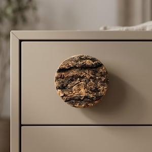 May include: A round, textured cabinet knob made from natural wood bark. The knob is brown and tan, with a circular shape and a rough, organic texture. It is mounted on a beige cabinet drawer.