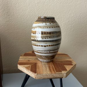 May include: A ceramic vase with a rounded body and a narrow opening, featuring horizontal bands of brown, tan, and white glaze with small dark brown dots and dashes arranged in repeating patterns around the exterior surface of the vessel.