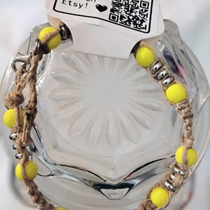 茶色の麻紐ブレスレット。黄色のマットな質感のビーズと銀色のディスクがあしらわれています。