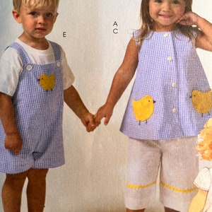 Peut inclure: Deux enfants, un garçon et une fille, portant des tenues assorties en vichy bleu et blanc avec des poussins brodés jaunes. Le garçon porte un t-shirt blanc sous sa salopette et la fille porte une robe sans manches. Les deux enfants se tiennent la main.