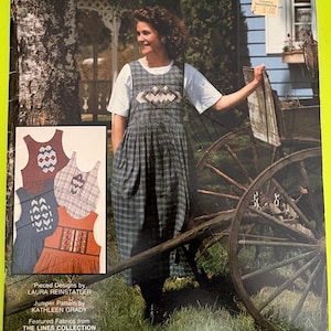 May include: A magazine cover for an "Artwear Jumper" pattern. The cover shows a woman in a plaid jumper over a white top. The jumper has an embroidered design on the bodice. The background includes a vintage wagon wheel and a blue house.