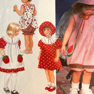 May include: A sewing pattern for a reversible dress and hat for a child. The dress has a red and white gingham pattern on one side and a white fabric with a fruit print on the other side. The hat is red with white polka dots.