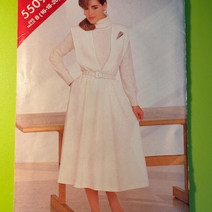 May include: A vintage sewing pattern titled "See & Sew 5509." The pattern features a woman wearing a white dress with a V-neck bodice, a belt, and a flared skirt. The pattern size is B (16-18-20). The background is a light green.