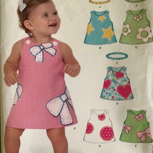 Könnte beinhalten: Ein Schnittmuster für Babykleider. Das Muster umfasst fünf verschiedene Stile: ein Gingham-Kleid mit einer großen Schleife, ein blaues Kleid mit Sternen, ein grünes Kleid mit Blumen, ein rosa Kleid mit Herzen und ein weißes Kleid mit Punkten. Das Muster enthält auch Anweisungen für die Herstellung eines Stirnbands.