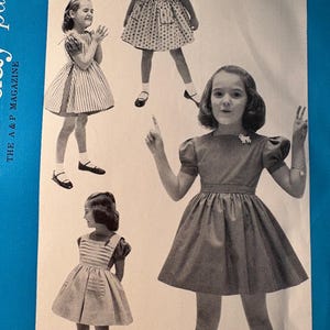May include: A vintage sewing pattern from The A & P Magazine, featuring four different styles of girls' dresses. The dresses are all in a simple, classic style, with a variety of fabrics and patterns. The pattern includes instructions for making each dress, as well as a list of materials needed.