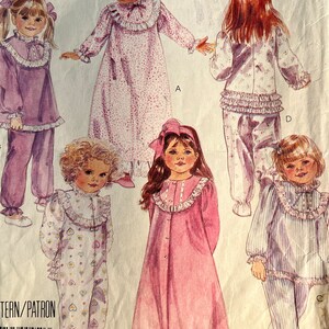 Può includere: Modello di cucito vintage McCall's con illustrazioni di pigiami per bambini. I modelli includono pigiami, camicie da notte e un pagliaccetto, tutti con colletti e polsini a balze. La tavolozza dei colori è tenue, con sfumature di rosa, lavanda e bianco.