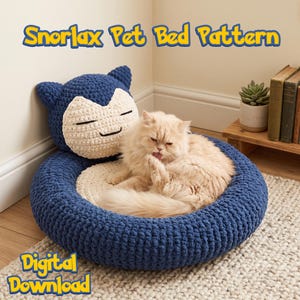 Puede incluir: Una cama para mascotas de ganchillo con un diseño de Snorlax en azul oscuro y crema, con una base circular y un reposacabezas elevado. El texto Snorlax Pet Bed Pattern y Digital Download es visible. Un gato color crema esponjoso está sentado en el centro.