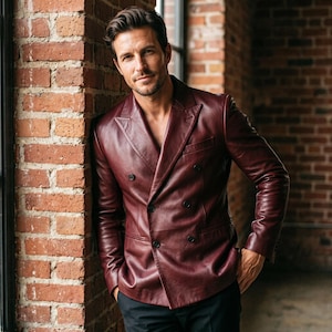 May include: A double-breasted blazer crafted from deep burgundy leather, featuring a notched lapel, long sleeves, and four dark buttons arranged in a two-by-two pattern. The garment has a structured fit with clean lines and a smooth finish.