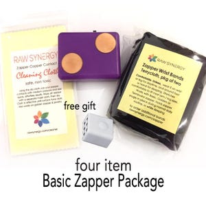 May include: A four item Basic Zapper Package containing a purple zapper with two copper contacts, a yellow cleaning cloth with Raw Synergy branding, a small grey cube, and a black terrycloth wrist band set in a clear plastic bag with a label.