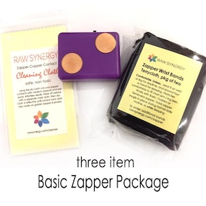 May include: A Basic Zapper Package with three items. Includes a purple zapper with copper contacts, a yellow cleaning cloth, and a package of black terrycloth wrist bands. The text on the package says "Zapper Wrist Bands Terrycloth, pkg of two."