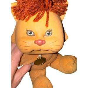 Peut inclure: Une poupée lion en peluche vintage avec un visage orange clair, une crinière en fil rouge et une petite étiquette dorée. La poupée a de grands yeux détaillés et un nez rose. Le lion est un jouet en peluche doux.