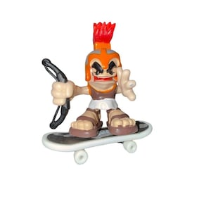 May include: A toy figurine of a gladiator with a red crest and orange helmet, holding a black bow and arrow, riding a skateboard. The figurine is wearing a white skirt and brown sandals. The skateboard is white with black detailing.