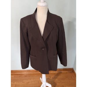 May include: A dark brown blazer with a notched lapel, single-button closure, and two front pockets. The blazer is displayed on a white mannequin. The jacket has long sleeves and a classic, tailored design.