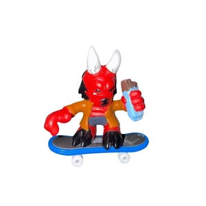 Puede incluir: Una pequeña figura de diablo rojo con cuernos blancos, cabello negro y una chaqueta marrón, sosteniendo un objeto azul y marrón. El diablo está montando una patineta azul con ruedas blancas. La figura tiene pezuñas negras.