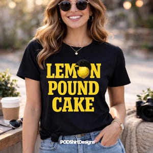 Puede incluir: Camiseta negra con las palabras "LEMON POUND CAKE" en letras amarillas. El diseño incluye un gráfico de limón. La camiseta la lleva una persona con gafas de sol y vaqueros azules.