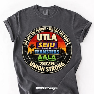 May include: Dark grey t-shirt with a circular graphic featuring text and a sunset design. The graphic includes "UTLA", "SEIU", "Teamsters", "AALA", and "Union Strong" with the year "2026". The shirt has rolled-up sleeves.