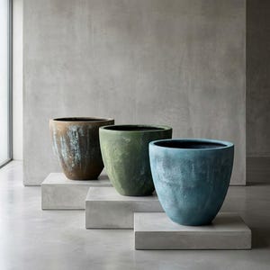 May include: Three large, textured planters in shades of brown, green, and blue. The planters have a wide, rounded shape and sit on concrete platforms. The background is a neutral gray.
