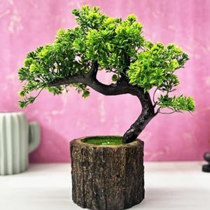 May include: An artificial bonsai tree with vibrant green foliage and a dark, textured trunk. The tree is planted in a cylindrical pot designed to resemble a natural tree stump with a rough, brown bark-like exterior and a green interior base.