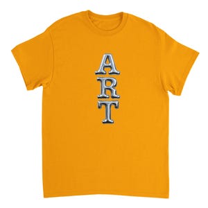 May include: Mustard yellow t-shirt featuring the word "ART" in a vertical, chrome-effect font. The letters are bold and contrast with the plain background. The shirt has short sleeves and a crew neck.