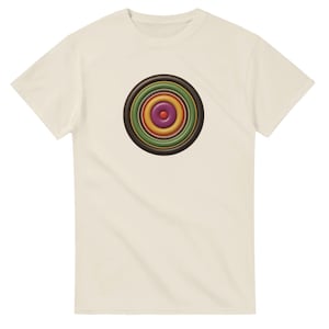 May include: A cream-colored short-sleeve t-shirt featuring a centered graphic of concentric circles. The design consists of a small red center dot surrounded by rings in shades of purple, yellow, green, and dark brown, creating a target-like pattern.