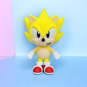 May include: A handmade yellow and tan crochet figure of a popular video game character. The figure has white eyes, a tan muzzle, and red and white shoes. The figure is standing on a light blue surface.