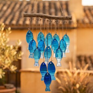 Peut inclure: Un carillon décoratif avec de nombreux poissons en verre bleu suspendus à une branche en bois. Les poissons, de différentes nuances de bleu, sont attachés avec de la ficelle, créant un thème côtier. L'arrière-plan est flou, suggérant un cadre extérieur.