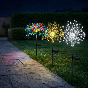 Op de afbeelding: Drie tuinlampen op zonne-energie op dunne zwarte staken, elk met een bolvormig vuurwerkontwerp met dunne draadvertakkingen. De lampen schijnen in veelkleurige, warmgele en koelwitte tinten en verlichten de donkere buitenruimte.