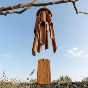 May include: A wooden wind chime with a natural finish hangs from a tree branch against a blue sky. The chime features several bamboo tubes and a rectangular wooden clapper. The overall design is simple and elegant, suitable for outdoor decor.