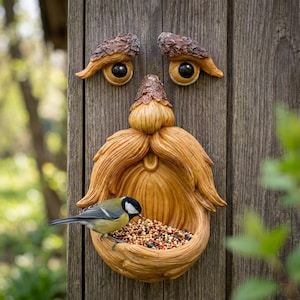 May include: A whimsical, wooden bird feeder shaped like a face with a long beard and large eyes. A small bird with yellow, black, and white feathers is perched on the feeder, eating seeds. The feeder is mounted on a wooden post.