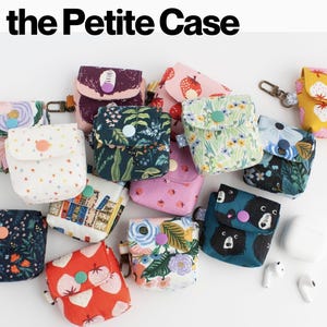 Puede incluir: Una colección de Petite Cases, pequeñas bolsas de tela con varios diseños, incluyendo florales, fresas y osos. Cada estuche tiene un cierre de botón. El texto "the Petite Case" se muestra en la parte superior.