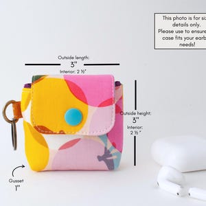 May include: A colorful fabric earbud case with a flap closure and a blue button. The case is 3 inches long, 3 inches high, and has a 1-inch gusset. The interior is 2.5 inches. The case has a key ring and is decorated with a vibrant floral pattern.