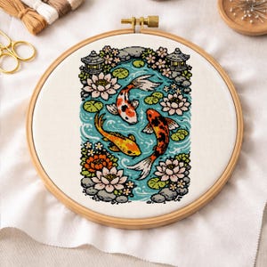 Könnte beinhalten: Ein Kreuzstich-Stickrahmen mit einer Koi-Teich-Szene. Das Design zeigt drei bunte Koi-Fische, die in blauem Wasser schwimmen, umgeben von Lotusblumen, Felsen und japanischen Laternen. Der Rahmen ist aus Holz.