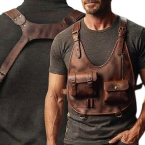 Könnte beinhalten: Ein Brustgeschirr aus braunem Leder mit verstellbaren Schulterriemen, einem großen Mittelteil mit zwei Vordertaschen, einem vertikalen Reißverschlussfach und zwei kleinen Schlaufen für Zubehör. Das Geschirr wird über einem dunkelgrauen T-Shirt getragen.
