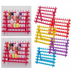 Puede incluir: Una colección de organizadores de carretes de hilo rojos, amarillos, morados y azules. Cada organizador tiene múltiples filas de clavijas para sujetar los carretes de hilo. Algunos organizadores están llenos de carretes de hilo coloridos.