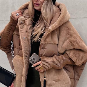 May include: A tan hooded jacket featuring a combination of smooth quilted panels and soft faux fur sections. The garment includes long ribbed knit sleeves in a matching tan shade, a front zipper closure, and snap buttons along the placket.