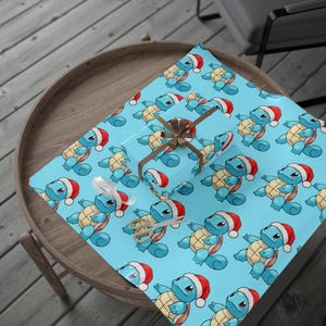 May include: A light blue wrapping paper featuring a repeating pattern of blue turtle characters wearing red and white Santa hats. A gift box wrapped in the same paper is tied with a brown ribbon, accompanied by a pair of metal scissors.