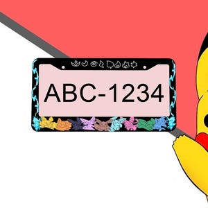 May include: Black license plate frame with the text "ABC-1234" in black. The frame has a light pink background and a border with blue accents. The bottom of the frame features colorful cartoon characters.