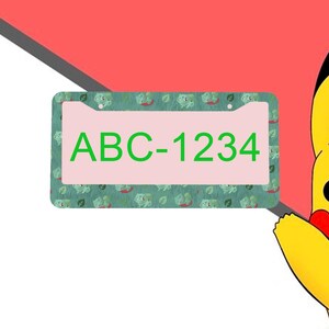 May include: A rectangular license plate frame featuring a repeating pattern of small green creatures and leaves on a dark green background. The center of the frame is light pink and displays the green text ABC-1234. A yellow character is visible.