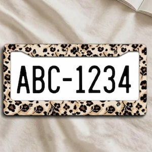 May include: License plate frame with a leopard print design. The frame surrounds a white license plate with the black text "ABC-1234". The frame has a tan background with brown spots and floral accents.
