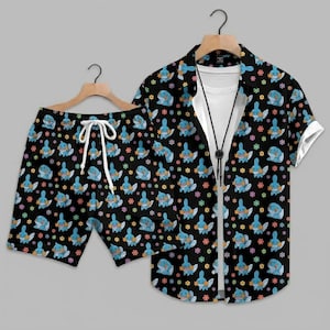 May include: A black short-sleeved button-down shirt and matching shorts set featuring an all-over pattern of small blue cartoon creatures and tiny multi-colored flowers. The shorts include a white drawstring at the waist for a secure fit.